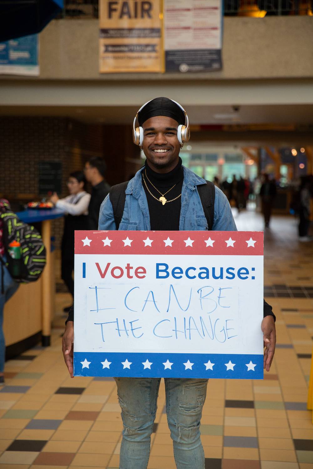 Student holding sign titled "I vote because: I can be the change"